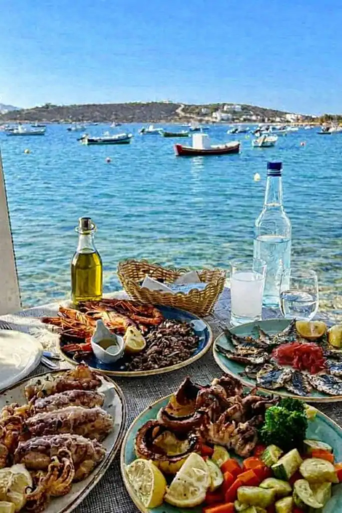 Τραπέζι με παραδοσιακά ελληνικά προϊόντα, όπως ελαιόλαδο και ξηρούς καρπούς, δίπλα στη θάλασσα.